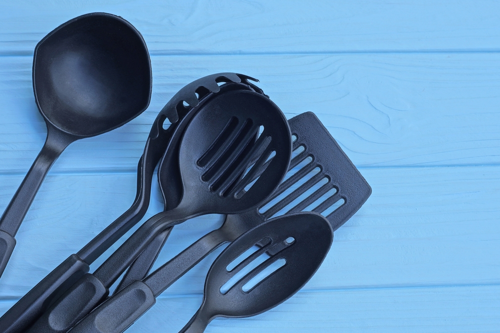 a heap of six black plastic kitchen utensils lie on a blue wooden table
