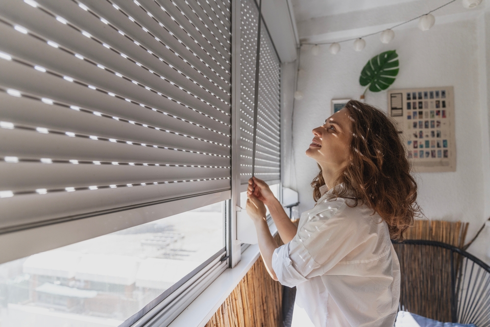 Young woman closing roller shutters on the balcony on a summer day