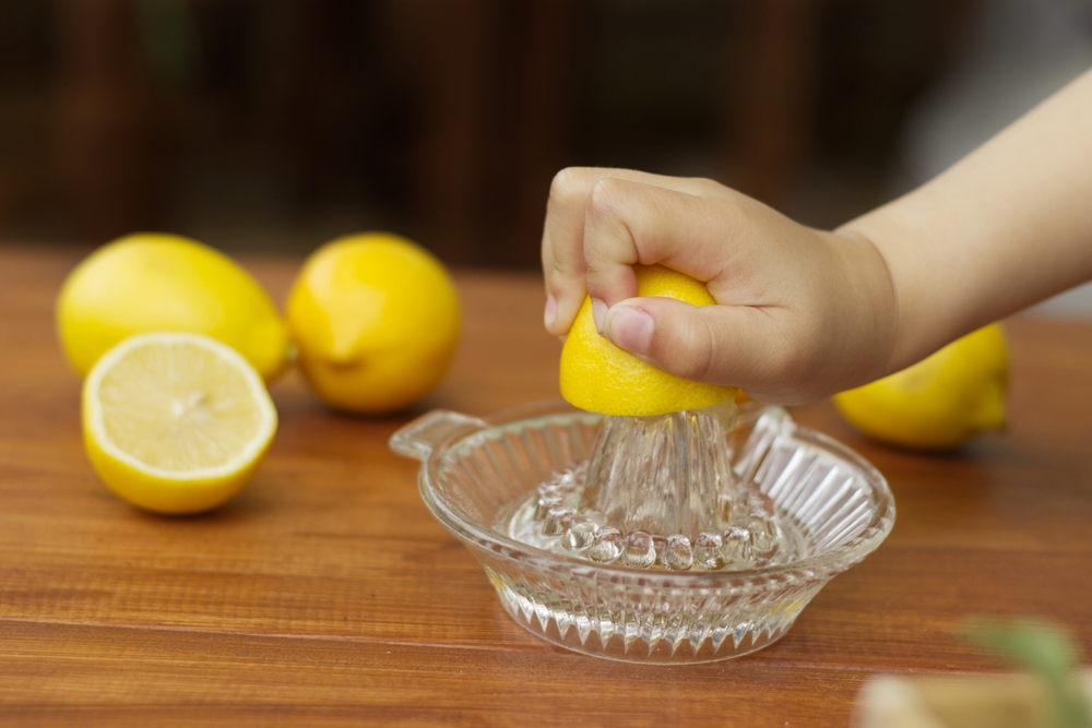 Little hand squeeze lemon juice with a lemon juicer glass on the wood table in the kitchen. Child prepare vegetable for a healthy cooking food vegetable concept.