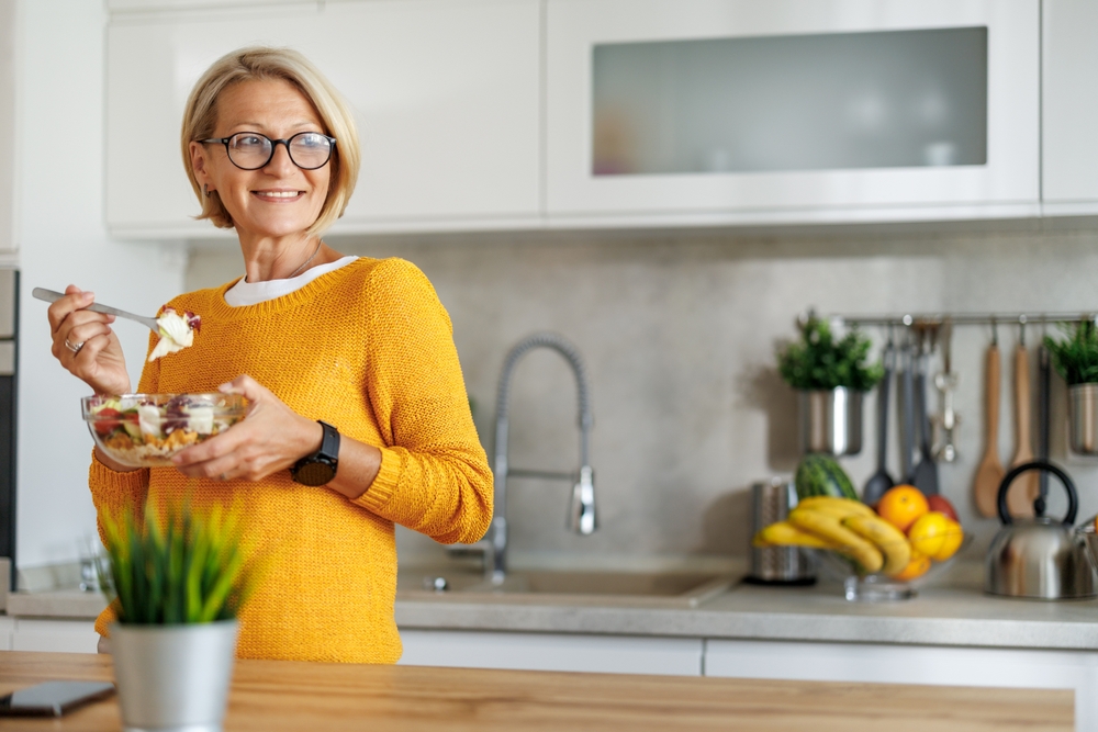 Attractive mature woman eating salads in her kitchen.Mature woman eating salads at home.