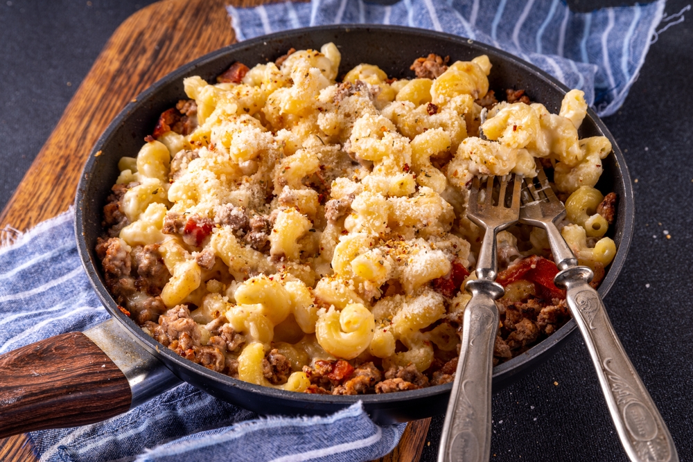 One skillet cheeseburger mac and cheese on frying pan, with macaroni pasta, a lot of cheese, bechamel sauce, ground beef meat and vegetables, tasty american food dish