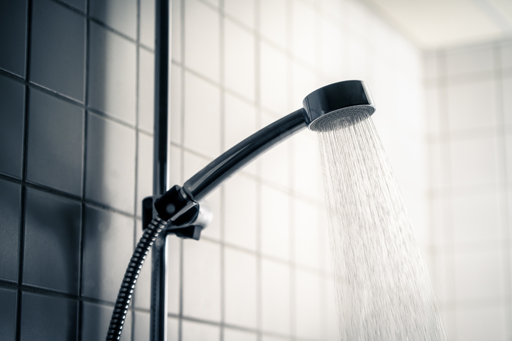 Shower head. Dark dramatic scary light. Cold water running in bathroom. Public washroom in hostel, gym or bad hotel. Hot flow. Black faucet. Emotional, horror or dirty. Wash room for bath.