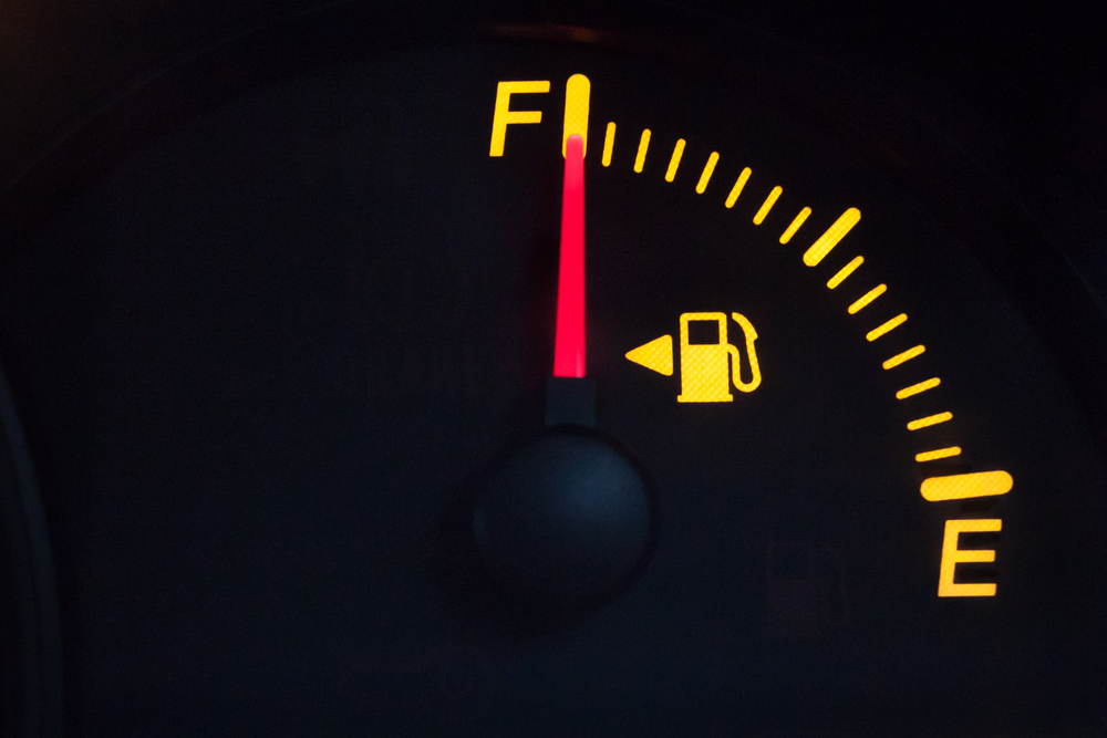 Fuel gauge showing a full tank. Yellow glowing meter with a red needle. Isolated against black background.
