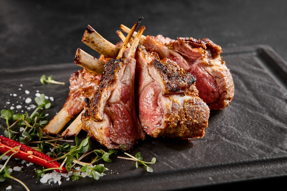 Perfectly grilled lamb rack served on a slate plate, with fresh herbs and a spicy red chili.