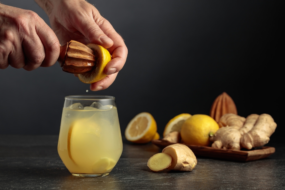 Ginger Ale with ice and lemon. Juice is squeezed out of a lemon with an old wooden juicer.
