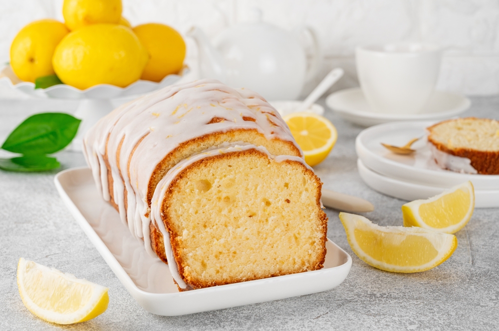 Lemon loaf cake with sugar icing on a white plate on a stone background. Copy space