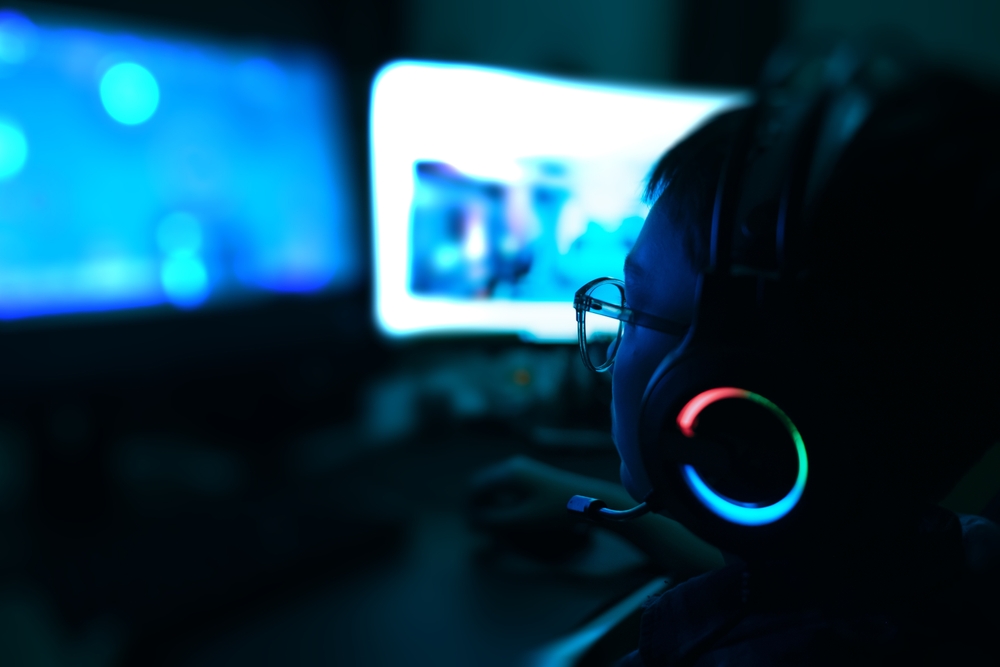 Young kid on the computer playing games, watching entertainment or browsing the online digital internet, young child wearing glasses and headset in the dark background theme.
