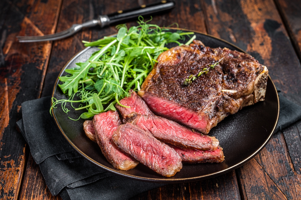 BBQ Grilled Wagyu New York beef meat steak or Striploin steak in a plate with salad. Wooden background. Top view.
