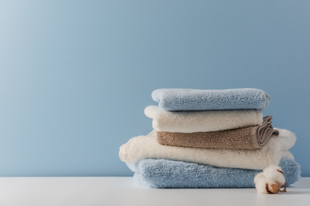 Stack of delicate colored cotton towels with cotton buds on blue background