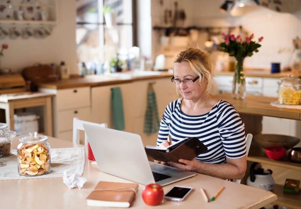 Older woman working from homeoffice. The retiree earning extra money during retirement. Woman paying bills online.