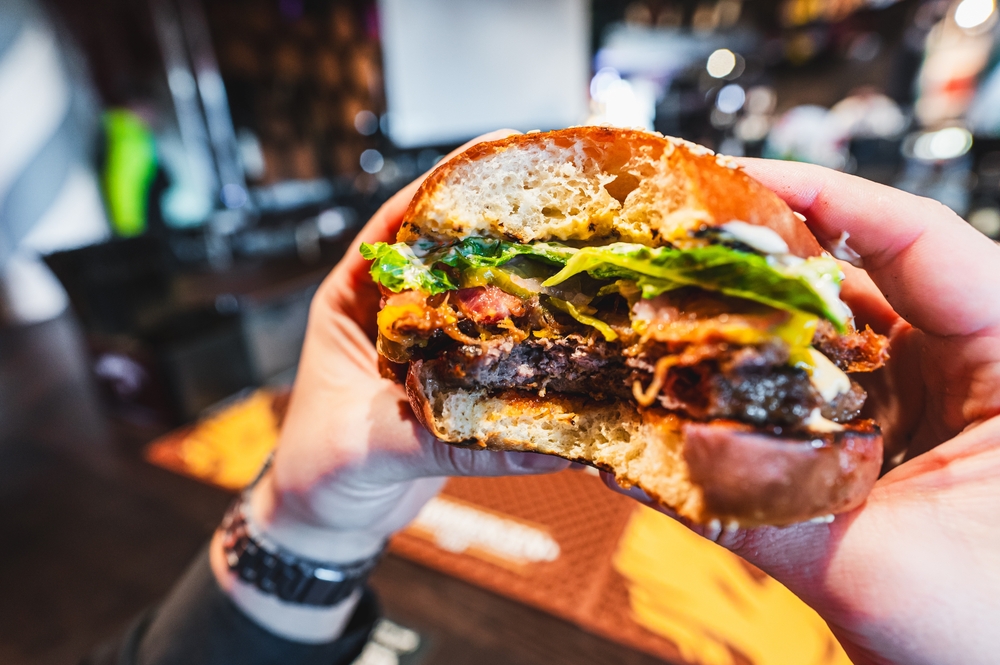 Close-up of a hand holding a half-eaten burger with lettuce and tomato, showcasing a casual dining experience.
