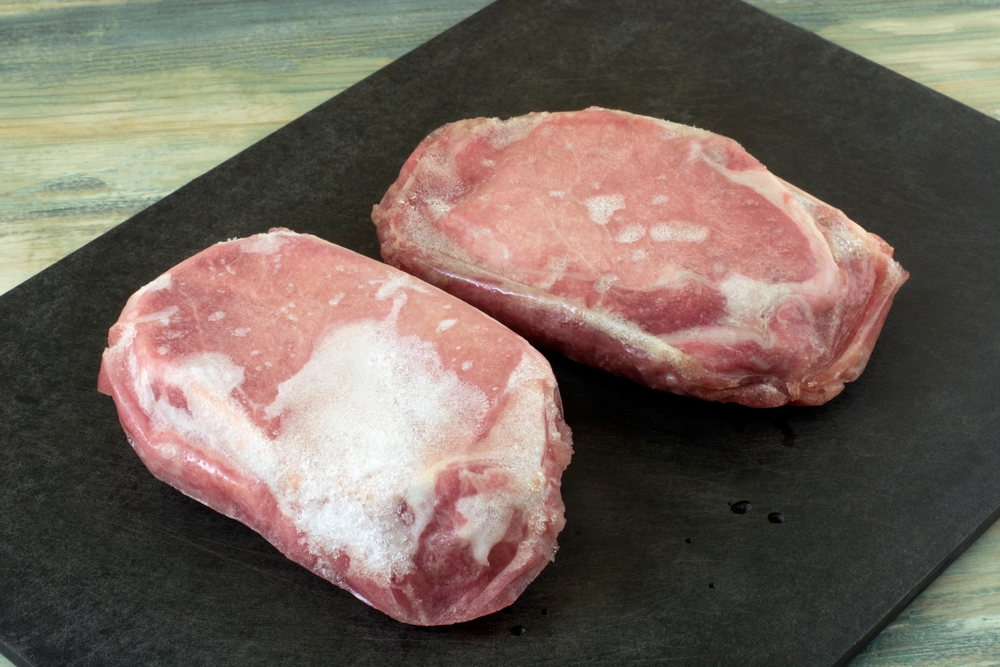 Two freezer burned boneless loin pork chops with ice crystals on black cutting board