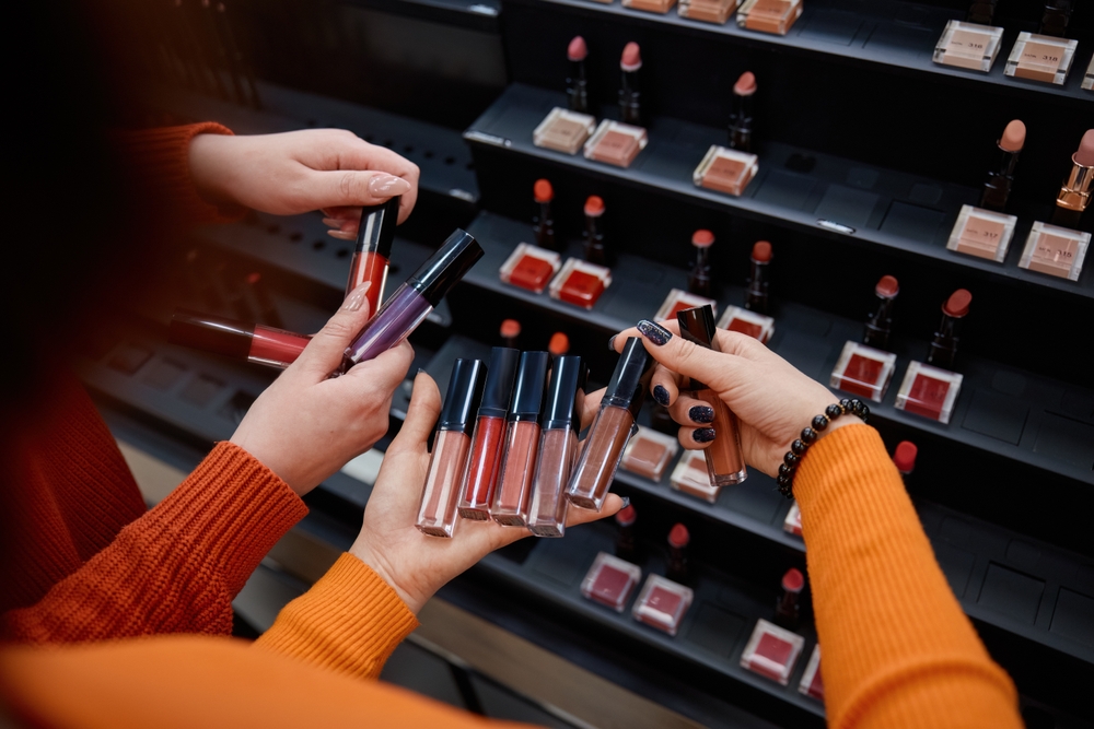 Womens hands holding lipsticks different colors in cosmetics shop
