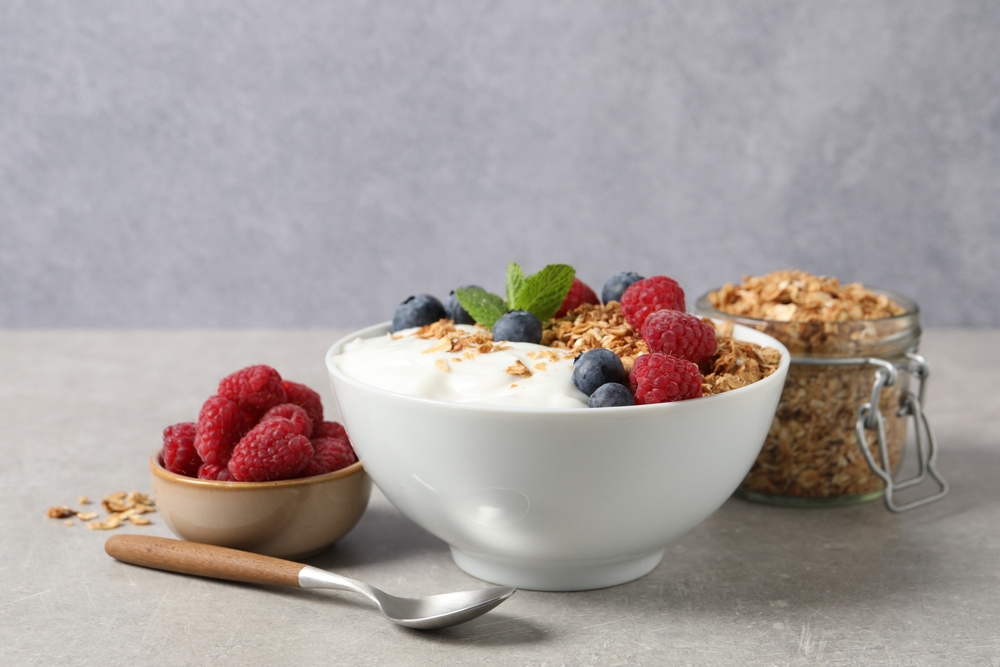Tasty granola with berries and yogurt in bowl on grey textured table, closeup
