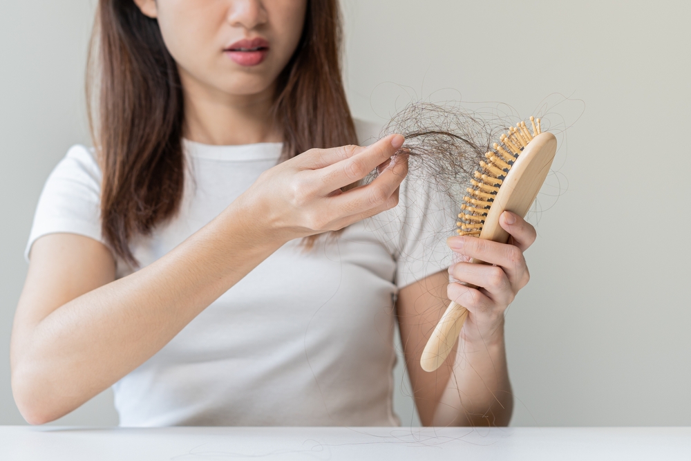Serious asian young woman holding brush holding comb, hairbrush with fall black hair from scalp after brushing, looking on hand worry about balding. Health care, beauty treatment, hair loss problem.
