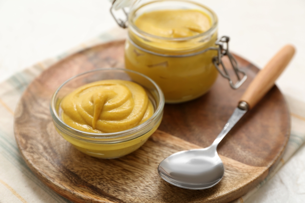 Board with jar of creamy mustard, spoon and bowl on white background, closeup