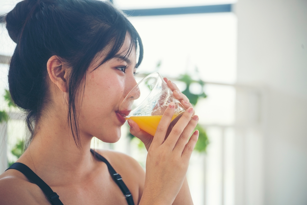 Asian women smile laugh look at camera health care home fitness lifestyle. Women hands holding cold orange juice fresh fruit cool drinking. Beautiful female pouring orange juice from cocktail bottle
