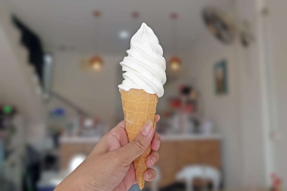 Hand holding Soft Serve Vanilla Ice Cream Cone with blurred cafe background. Selective focus.
