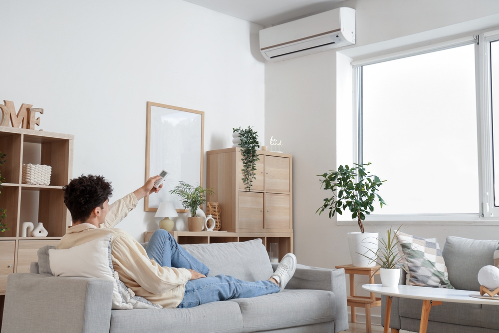 Young man resting on sofa in room with operating air conditioner