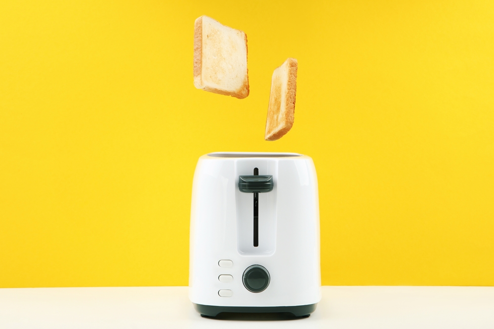 Roasted toasts jumping out of the toaster on yellow background