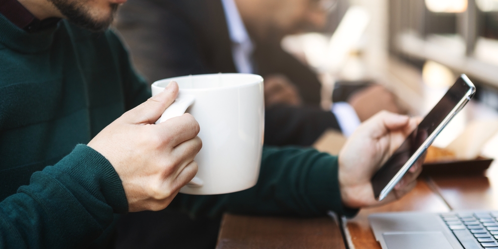Person holding a large coffee mug while using a smartphone at a cafe. Casual setting with focus on coffee and phone. Business professional, business corporate concept.
