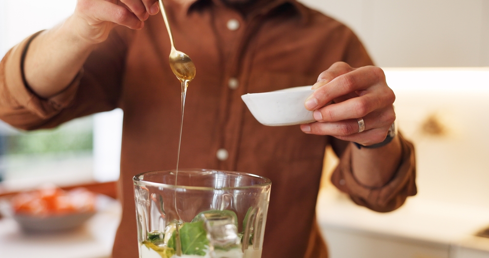 Person, kitchen and hands with ingredients in blender for healthy smoothie, breakfast drink and gut health. Spoon, detox and honey in home for shake preparation, organic diet and natural antioxidant
