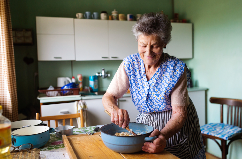 Senior woman baking pies in her home kitchen. Mixing ingredients.

