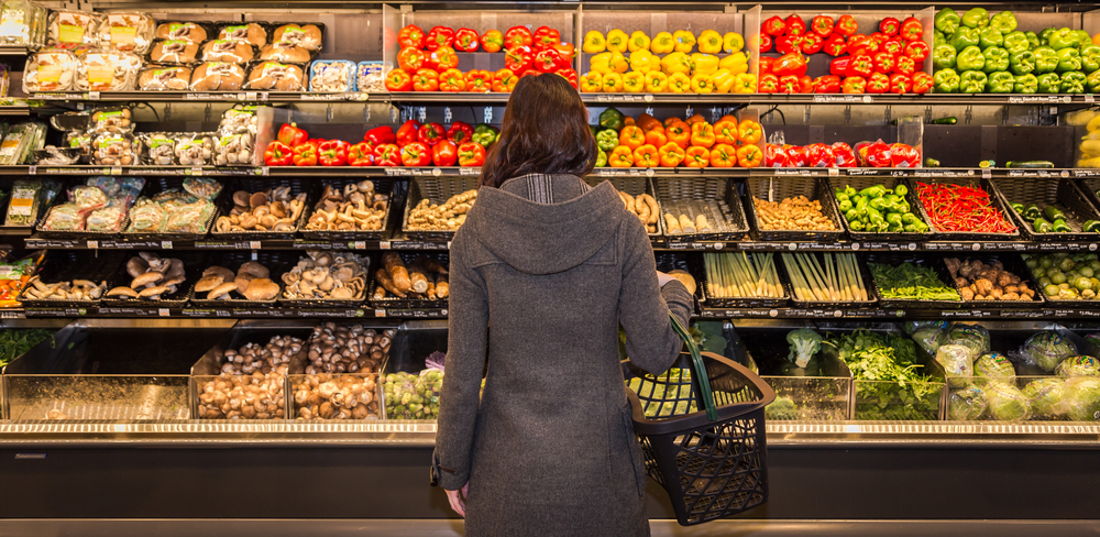 Woman standing in front of a row of produce in a grocery store. 