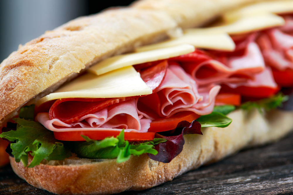 Sandwich with lettuce, slices of fresh tomatoes, salami, hum and cheese