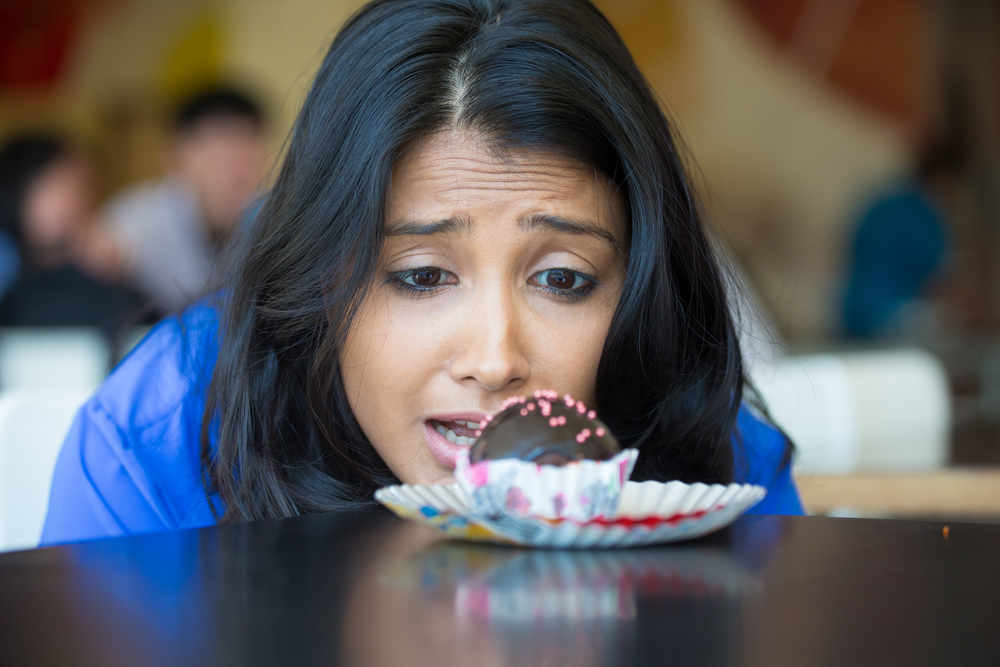 Closeup portrait of desperate woman in blue shirt craving fudge with pink sprinkles dessert, eager to eat, isolated indoors background