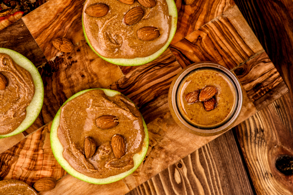 Granny Smith apples with smoothie almond butter with whole almond on the top. Healthy appetizers Apples with peanut butter on the wood table background. Top view snack on