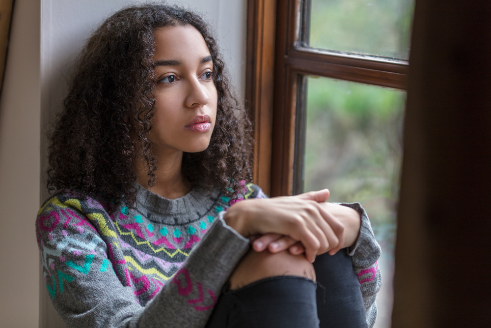 Beautiful mixed race biracial African American girl teenager female young woman sad depressed or thoughtful looking out of a window