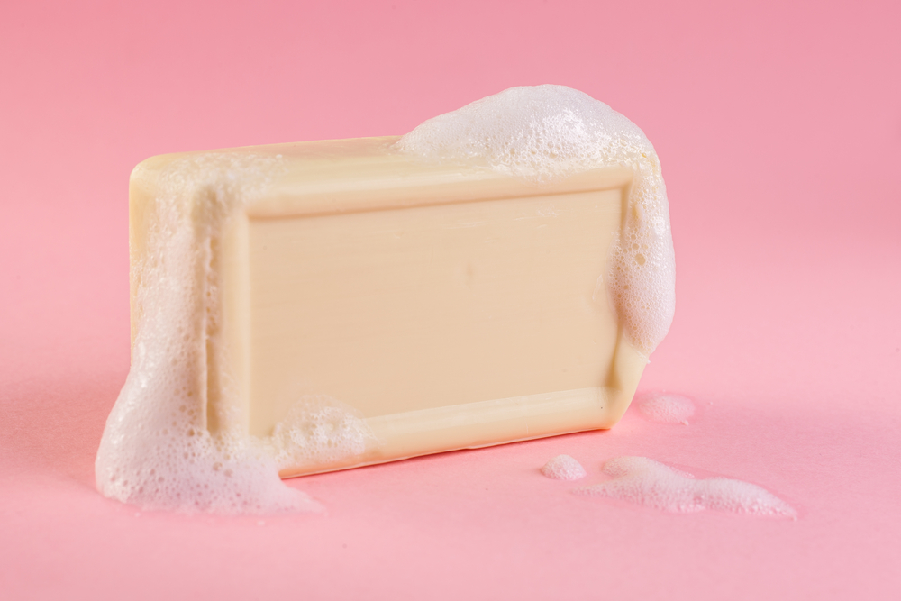 yellow soap bar in foam with copy space in center isolated on bright pink background
