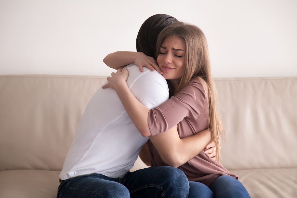 Portrait of emotional young couple hugging each other tightly, boyfriend and girlfriend embracing sitting on couch, reconciliation after argument, love you so much, strong affection in relationships