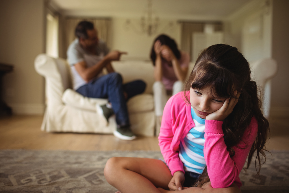 Sad girl listening to her parents arguing at home