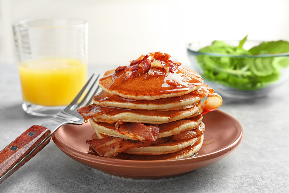 Plate with pancakes and bacon on table
