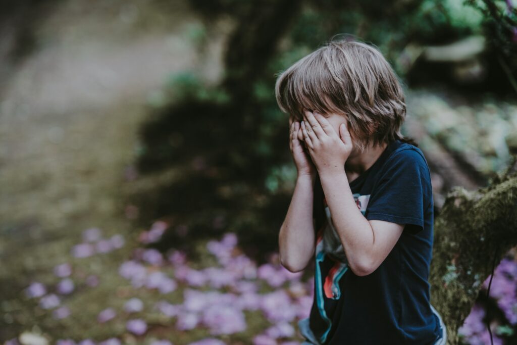 boy covering his face while standing

