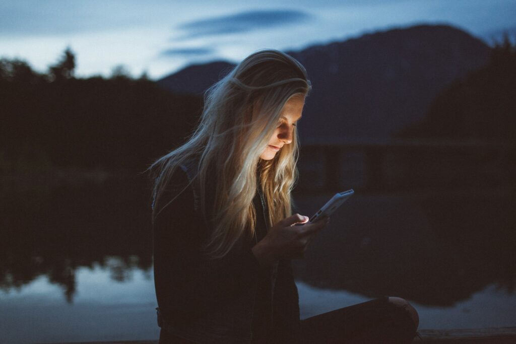 woman looking at phone beside body of water
