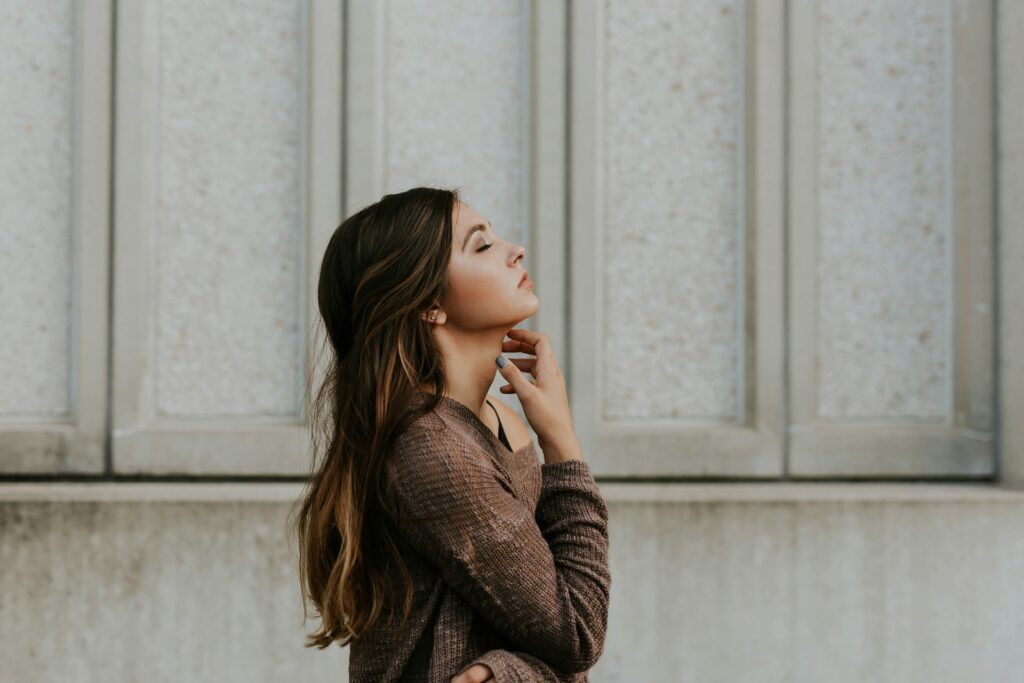 woman in brown long-sleeved top standing beside wall
