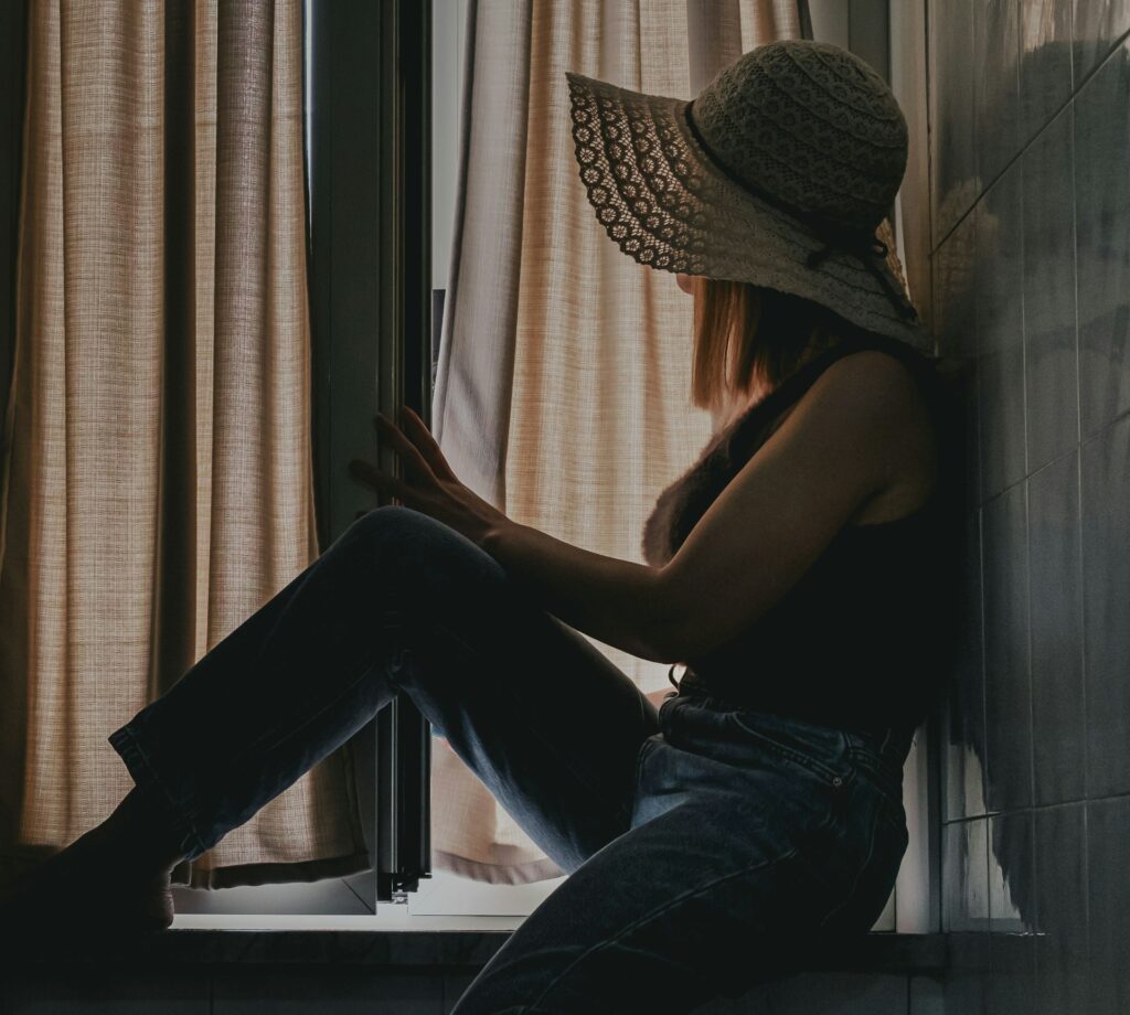 woman in black tank top and blue denim jeans sitting on window
