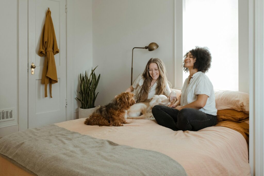 woman in white long sleeve shirt sitting on bed beside brown dog
