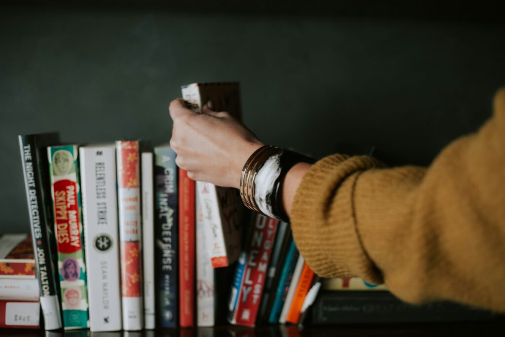 person picking white and red book on bookshelf
