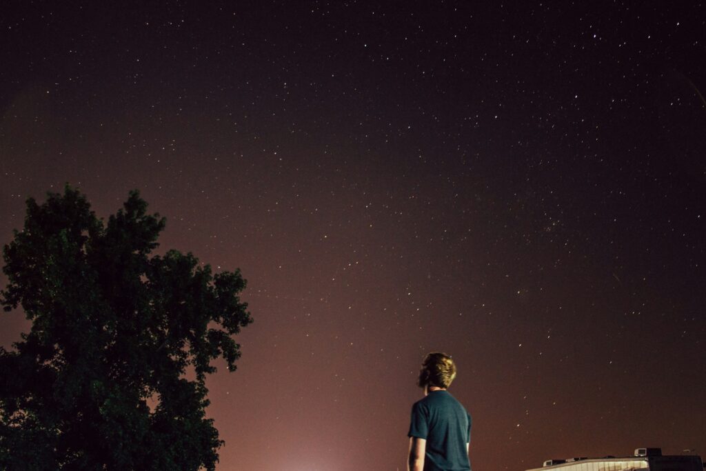 man standing beside tree under brown sky
