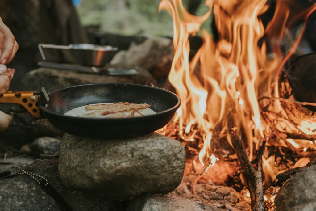 a person cooking food over a skillet over a campfire
