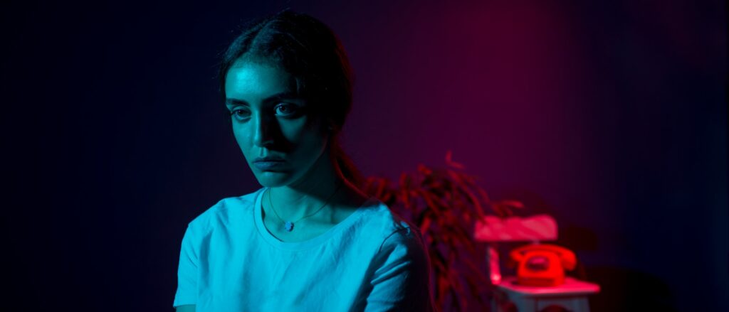 a woman sitting in a dark room next to a plant

