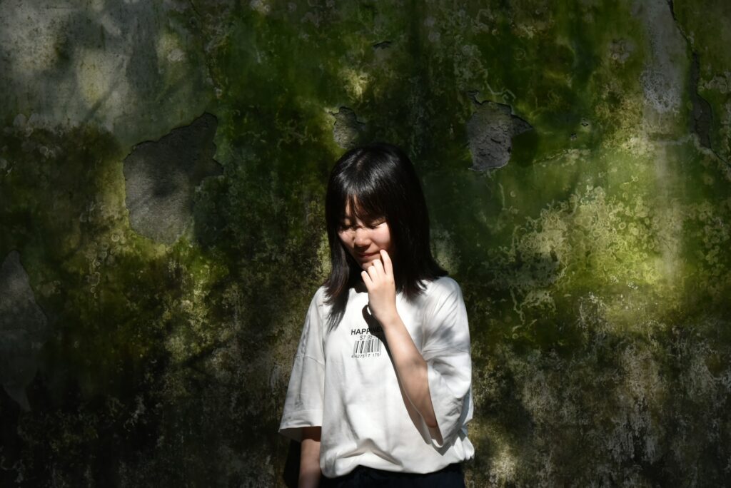 a woman standing in front of a moss covered wall