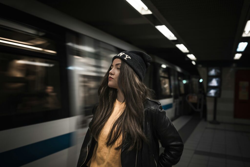 woman putting her hand on jacket pocket while standing beside train at station

