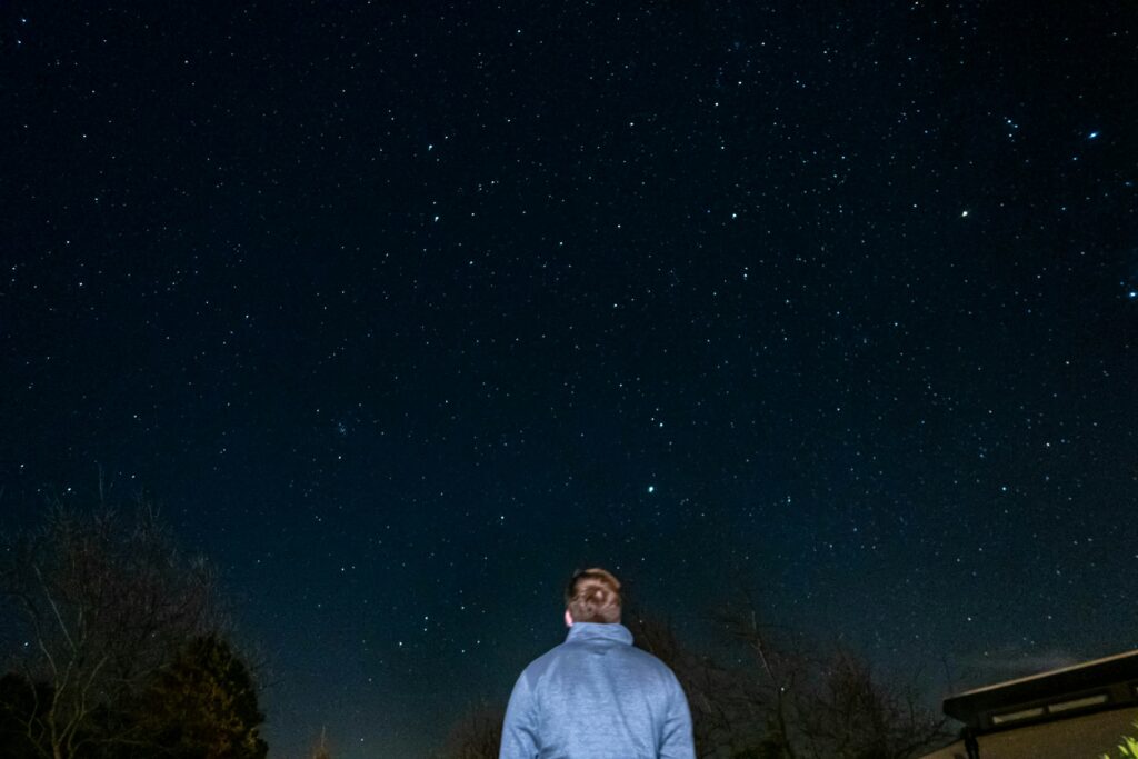 a man standing in the grass looking up at the stars
