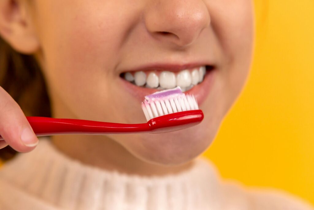 girl with red and white toothbrush in mouth
