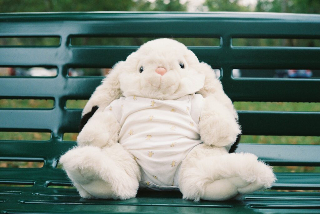 a white stuffed rabbit sitting on top of a green bench
